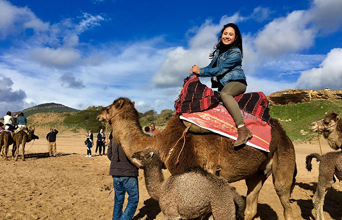 Gina Bolanos smiling at the camera while riding a camel.