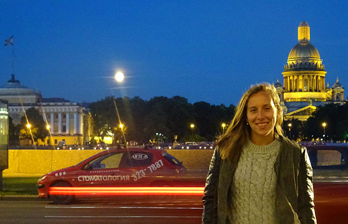 Siobhán Seigne posing for a night photo in St. Petersburg with a car and buildings in the background.