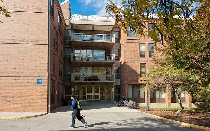 A student walks in front of the entrance to Gale House with a tree in the foreground
