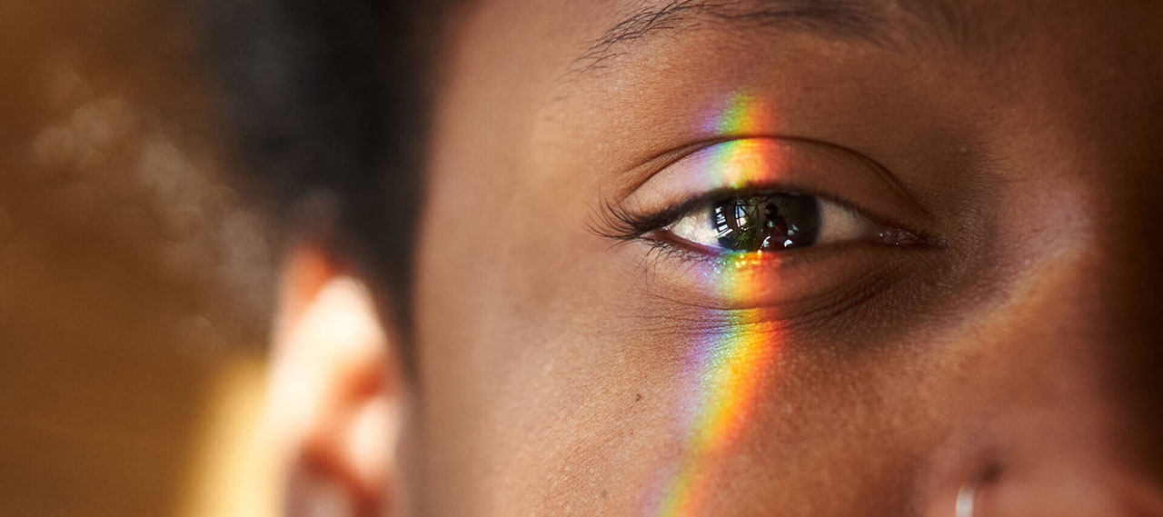 Close-up of a Black person's eye with a multicolored light falling on it to illustrate how retinal ganglion cells function.