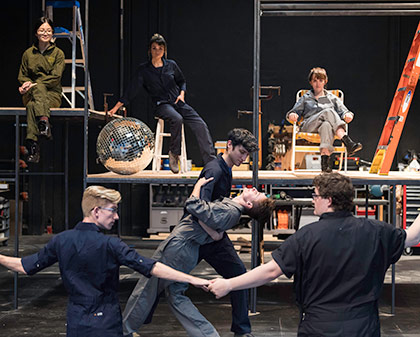 actors in jumpsuits in front of, and on, construction platforms