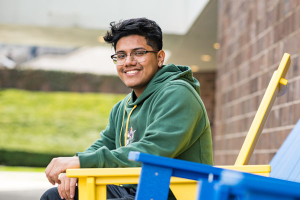 University of Rochester Student, Justin Pimentel ‘23, a computer science/history double major and first generation student from the Bronx, sitting on a yellow chair on campus.