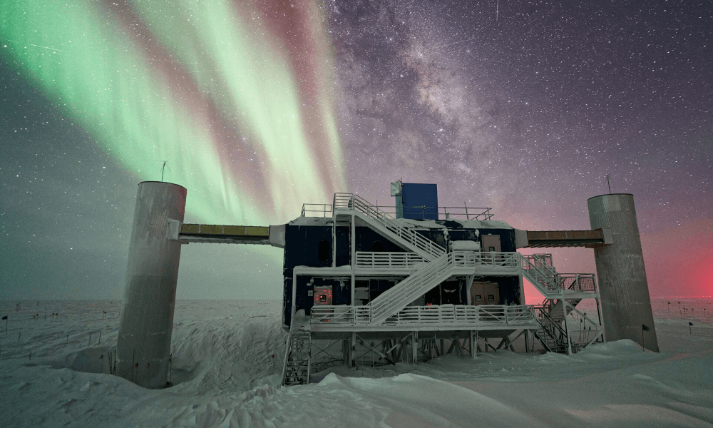 IceCube Neutrino Observatory at night with the Northern Lights in the sky.