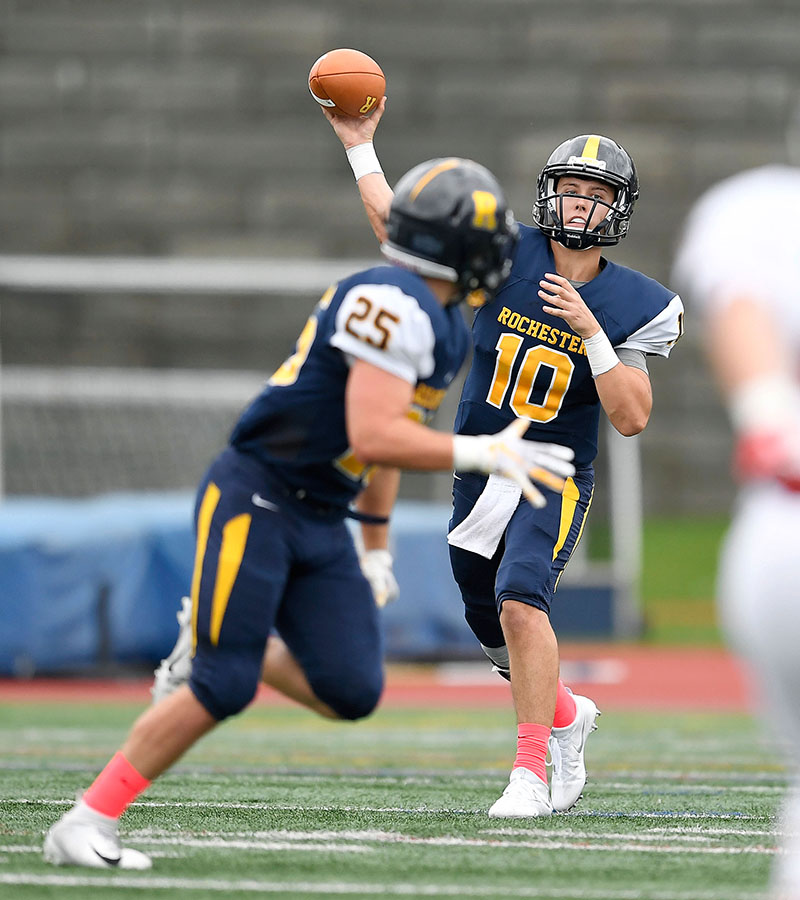 A football player in uniform throws a forward pass to a teammate.