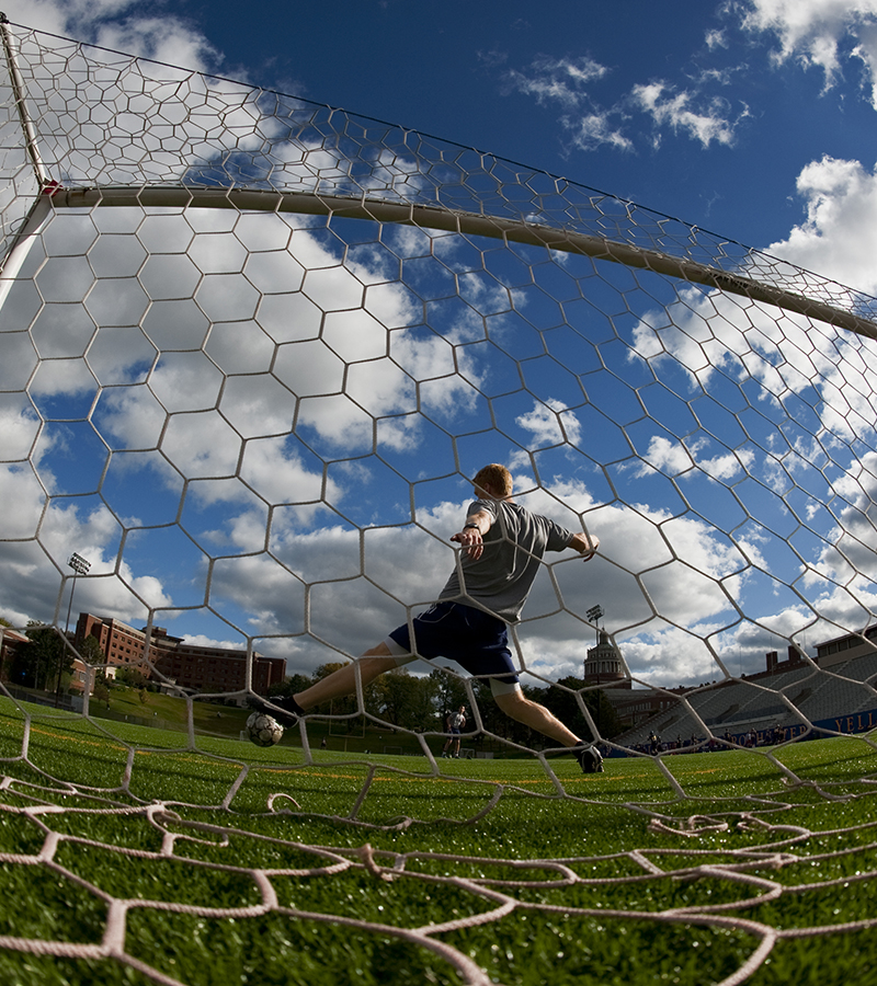 A student attempts to stop a soccer ball from entering the net as seen from behind the net.
