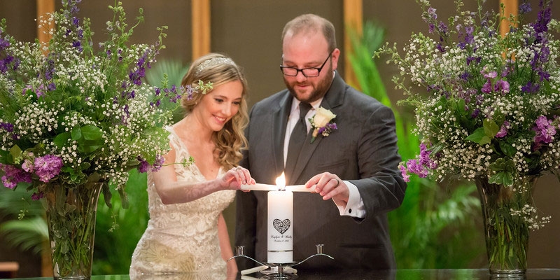 A bride and groom lighting a candle together.