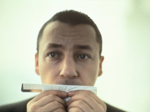 Screenshot of Three Colors: White. A man holds a comb, looking past camera.