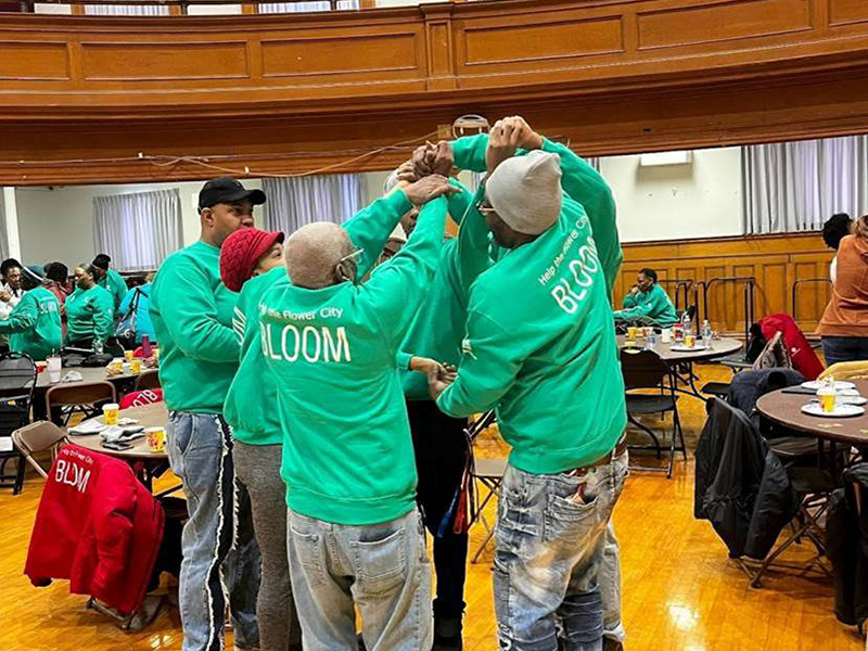 A group of people wearing green sweatshirts holding their arms up together.