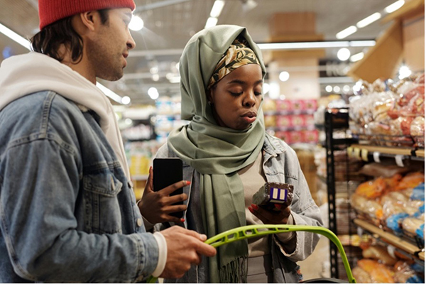Two people standing in a grocery store looking at a handheld device.