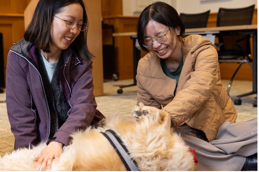 Two students smiling while petting a furry dog.