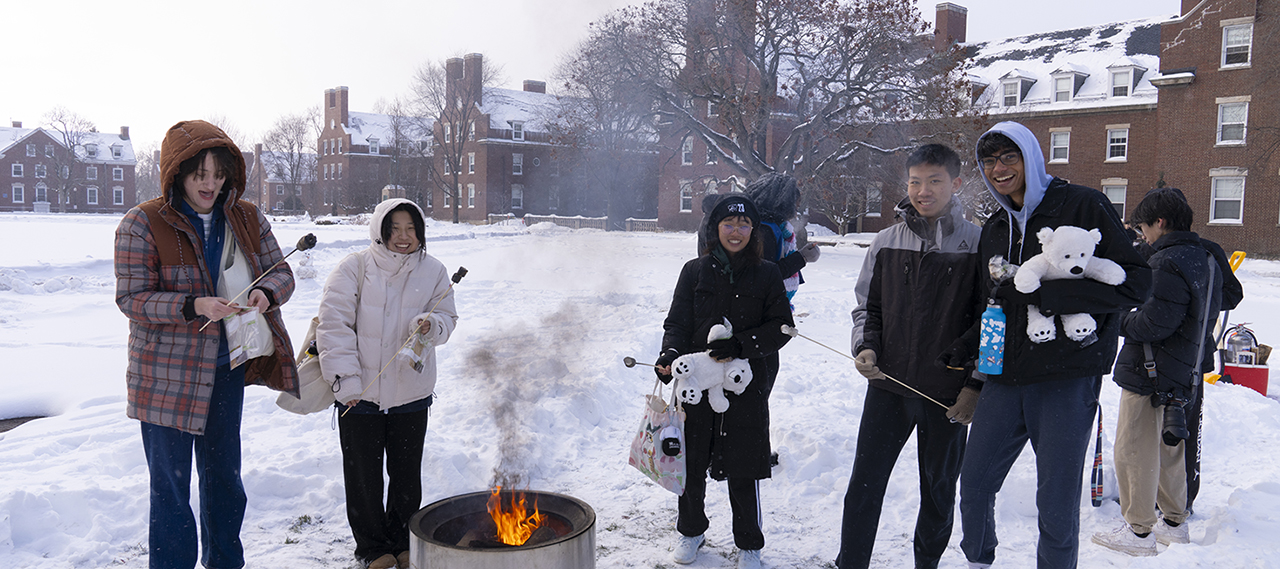 Cold and bundled up students pose for the camera while making s’mores and holding stuffed animals outside in the snow during winter fest weekend.