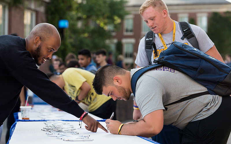 Photo of a staff member helping a student sign their class roll at a past Convocation ceremony during Fall Welcome Week