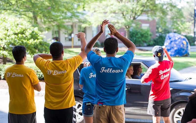 Photo of several student volunteers cheering as a car pulls up to a residence hall during new student move-in