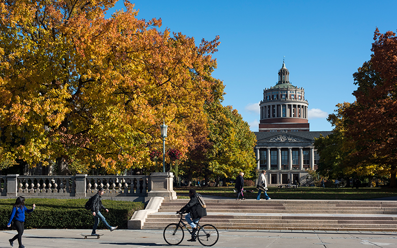 Photo of students walking and biking in front of Eastman Quad on campus