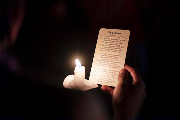 Photo of The Genesee lyric card held by a student and lit by a candle