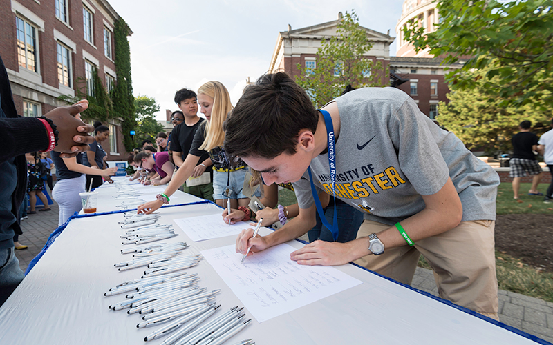 Photo of a student leaning over a table to sign their class roll at Convocation during Fall Welcome Week