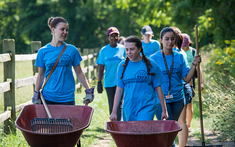 Photo of students pushing a wheelbarrow and carrying gardening equipment