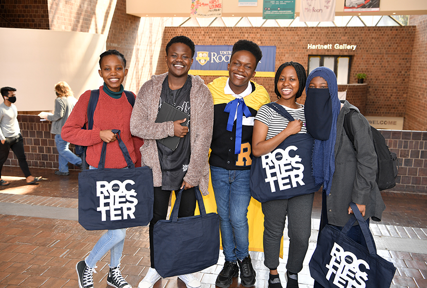 Photo of students posing in Wilson Commons, holding University of Rochester tote bags