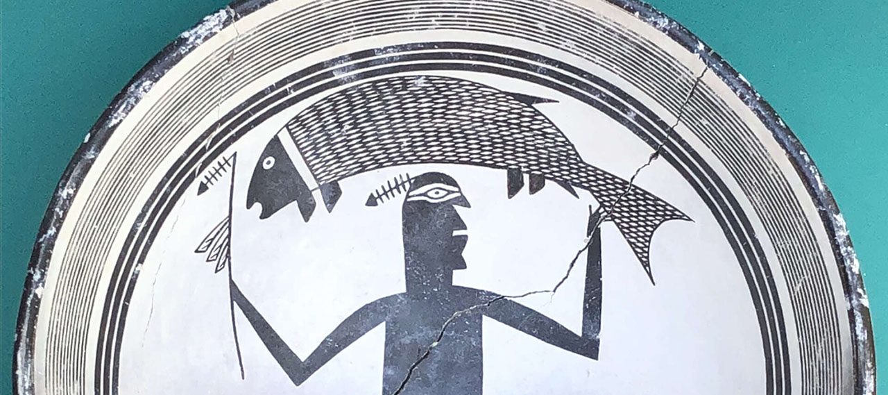 Close-up of a Native American art replica Mimbres bowl featuring a geometric figure holding a fish aloft.