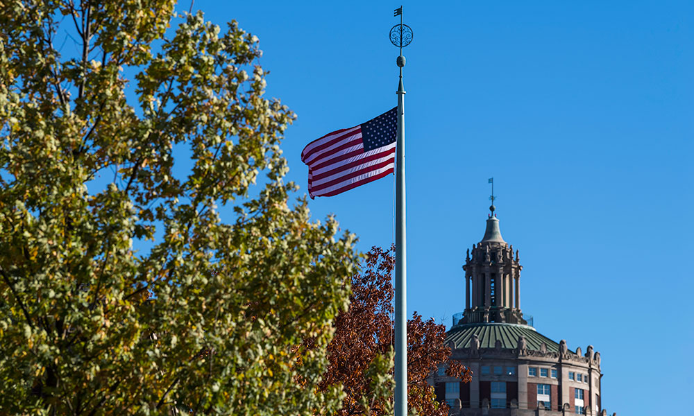 An American flag flying in front of Rush Rhees library on a clear day.