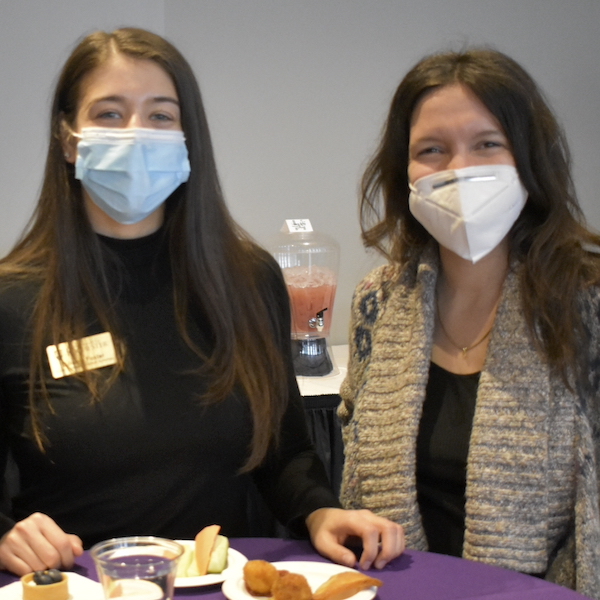 Two masked women smiling together in front of small plates of food