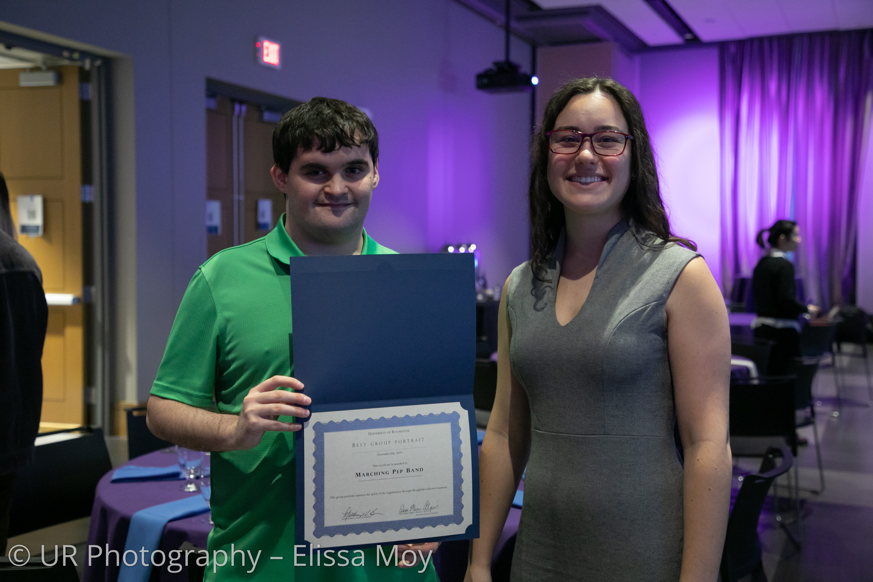 Two students posing with one presenting a certificate