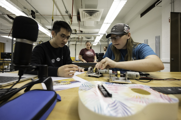 Two students in foreground examine ball bearings in a lab