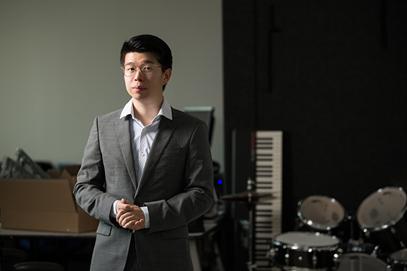 Neil Zhang stands in the AIR Lab with a keyboard and drums in the background.