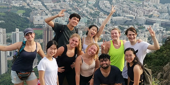 A group of students pose for a photo atop a hill with Hong Kong in the background.