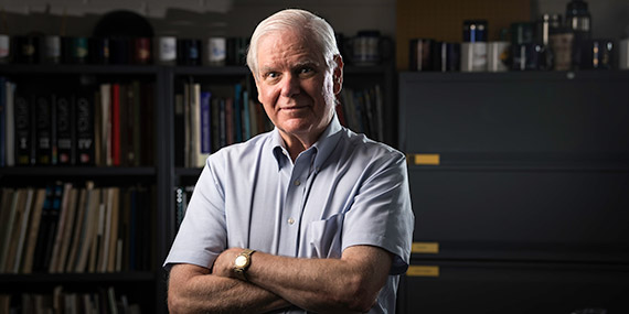 James Fienup poses with his arms folded in his dimly lit lab