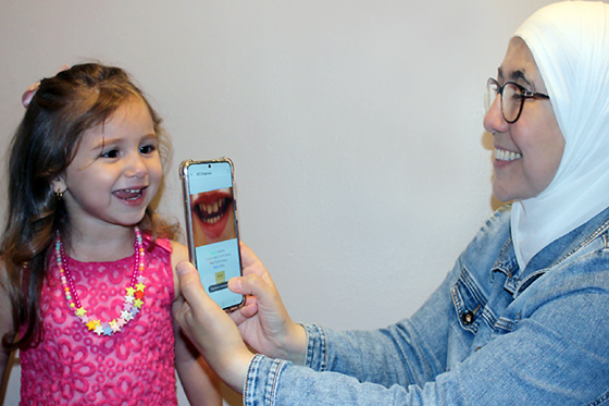 An adult takes a photo of a child's smile using a smartphone.