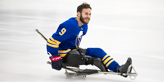 Sam Becker smiles and glides across the ice rink in a Sabres uniform, mounted on a hockey sled.