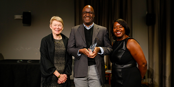 Marvin Doyley, center, holds a glass award while Sarah Mangelsdorft, left, and Adrienne Morgan stand beside him.