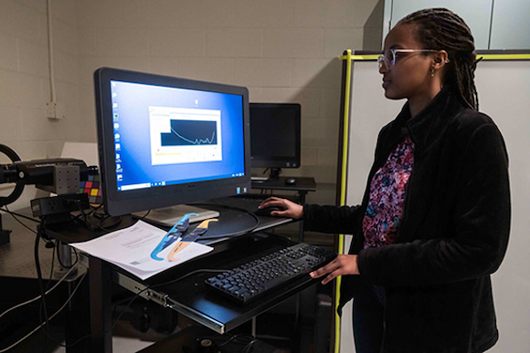 students stands beside a computer terminal with her hand on the mouse.
