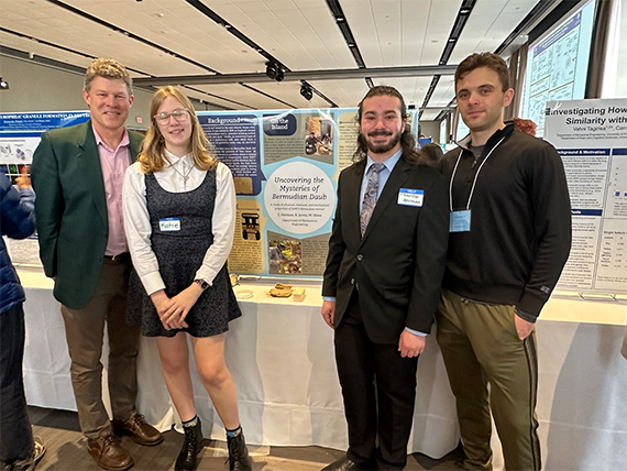 Michael Jarvis, Katie Jarvis, Charlie Herman, and Will Shaw pose in front of a poster at the Undergraduate Research Expo.