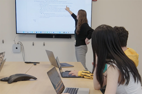 Assistant Professor Caitlin Dreisbach points at a screen while data science students look on.
