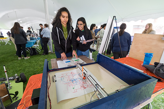 Students examine a project while standing inside a tent during Design Day.