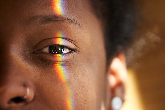 An extreme close-up of a person's face with a rainbow crossing over the eye.