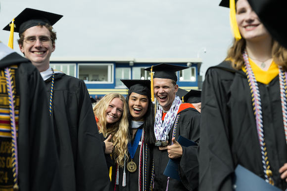Five students smiling, in graduation regalia
