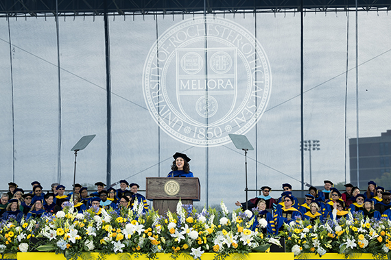 Raquel Ajalik speaks at the podium during the University of Rochester commencement ceremony at Fauver Stadium.