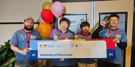 Three students and their coach hold up a placard at the ICPC contest celebrating their strong placement.