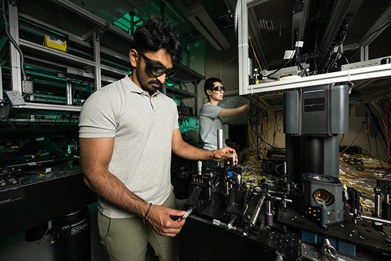 Two researchers wearing protective eyewear manipulate equipment in an optics lab to produce surface acoustic waves.