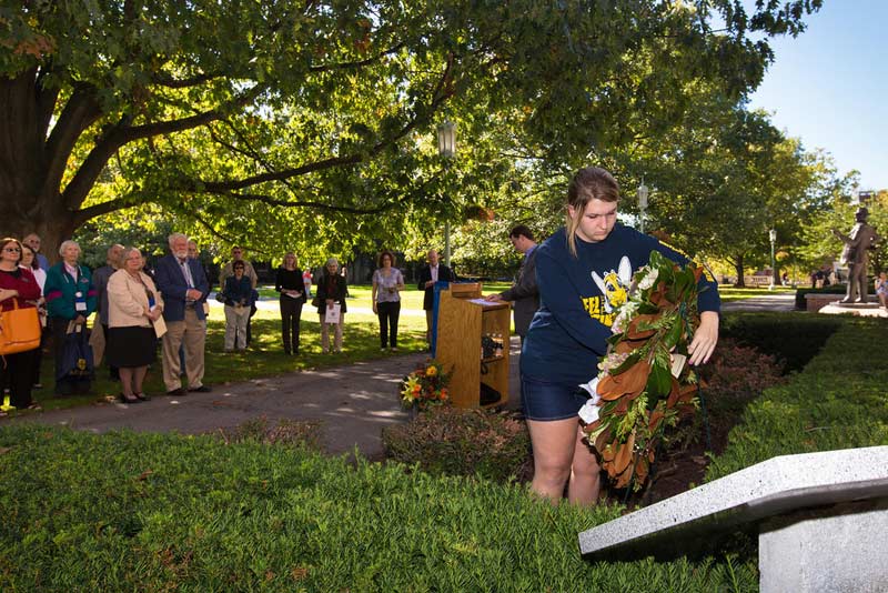 student lays a wreath at a memorial stone