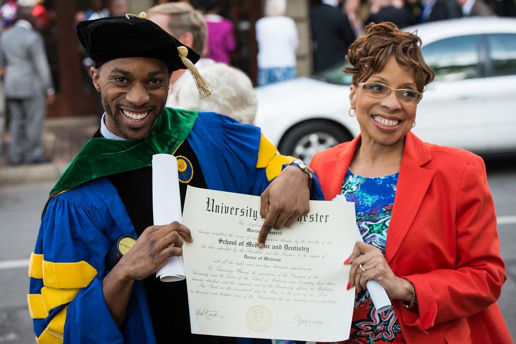 smiling student with his mom points to his diploma