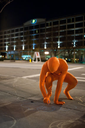 Orange Man writes in chalk on sidewalk