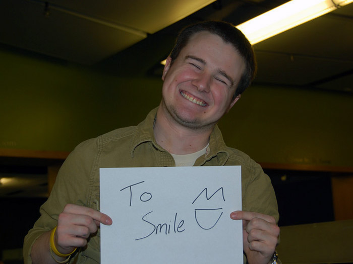 student holding sign that reads TO SMILE