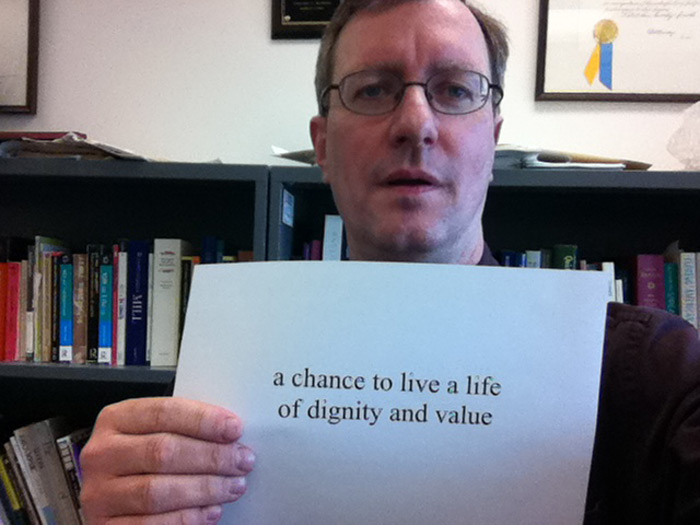 student holding sign that reads A CHANCE TO LIVE A LIFE OF DIGNITY AND VALUE