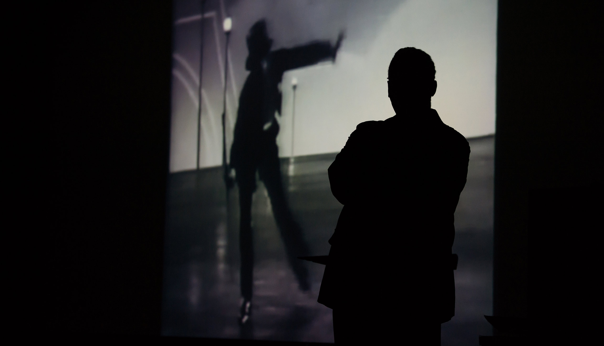 Paul BUrgett casts a shadow on a movie screen showing jazz musicians