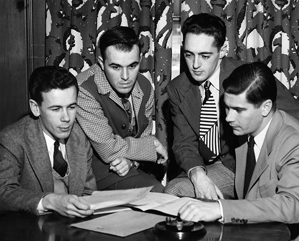 yearbook photo of four men reading papers at a desk