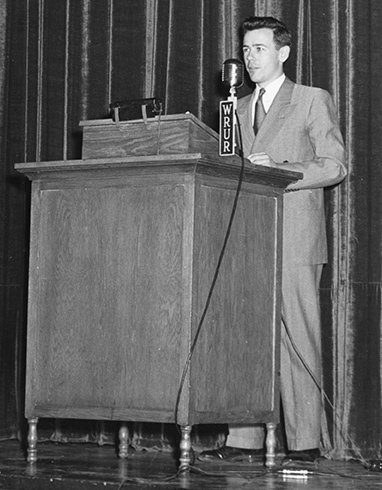 historic yearbook image of  man standing behind a podium with a banner that reads WRUR